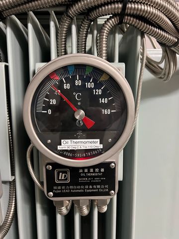 Close-up of an oil thermometer with temperature gauge and metal tubes.