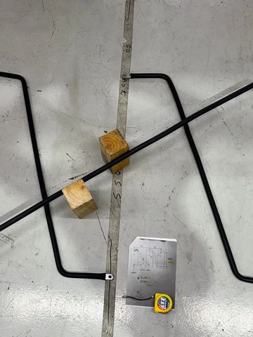 Two black metal rods on a workshop floor with wooden blocks and a tape measure.