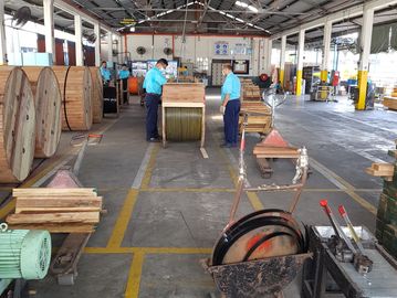 Workers handling large cable reels in a spacious industrial warehouse.