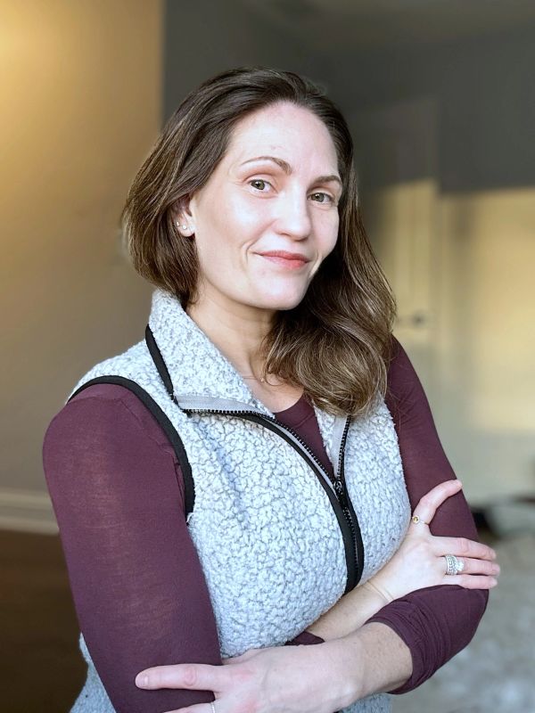 Woman with folded arms wearing a light blue fleece vest.