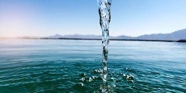 Clear water pouring into a calm lake under a blue sky.
