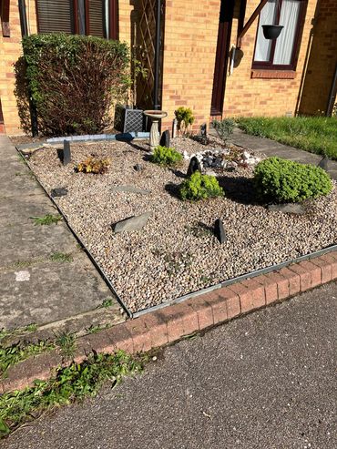 Small front garden with pebbles, plants, and a birdbath.