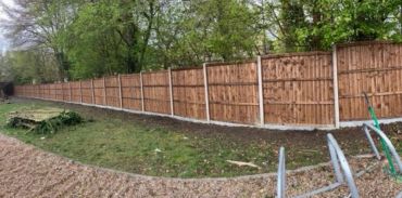 Long brown wooden fence in a garden area.