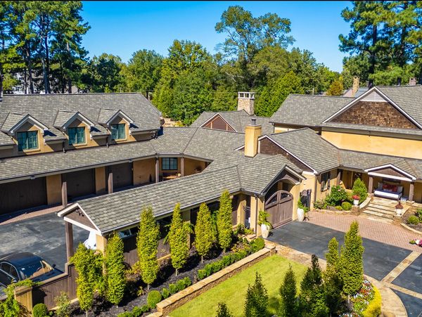 A large, elegant house with a manicured garden and multiple roof sections.