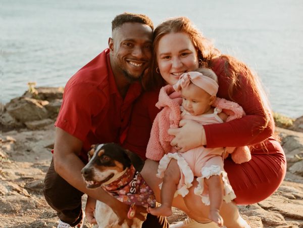 One man wearing red shirt, one woman wearing red dress and smiling, baby girl, and a dog