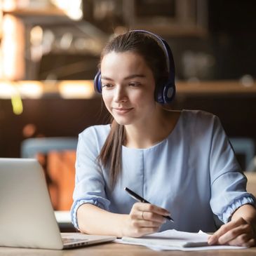 Focused woman wearing headphones using laptop in cafe, writing notes
