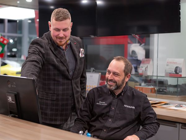 Two men in a Nissan dealership discussing something on a computer.