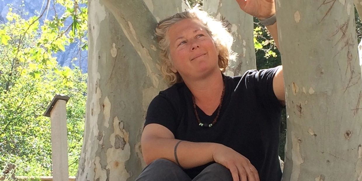Woman sitting and smiling outdoors near trees.