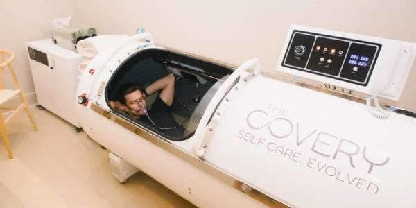 Man relaxing inside a white hyperbaric oxygen therapy chamber.