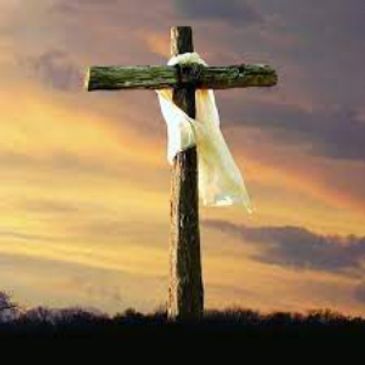 Wooden cross with white cloth against sunset sky.
