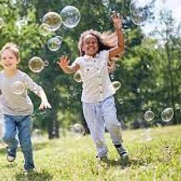 Two children running and playing with bubbles outdoors.
