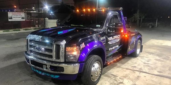 A customized purple tow truck with bright orange lights parked at night.
