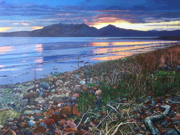 Sunset over a rocky shoreline with mountains and reflective water.