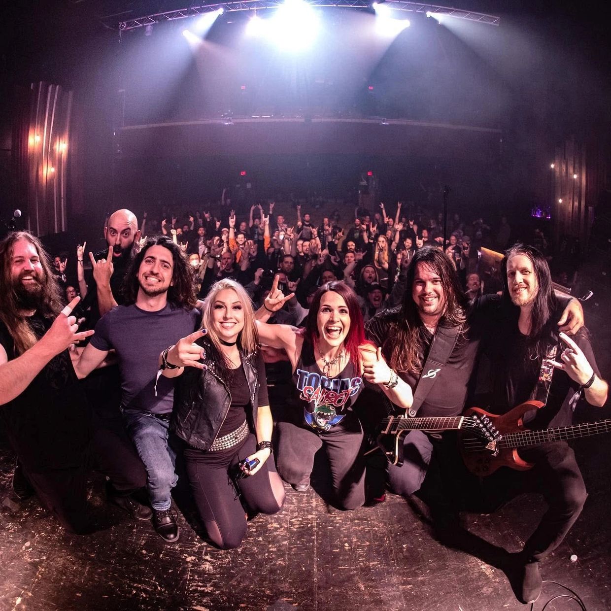 A lively rock band poses with their enthusiastic crowd after a concert.