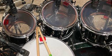 Close-up of a drum set with drumsticks resting on the snare drum and cymbals above.