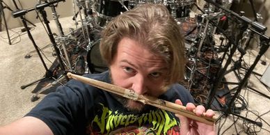 A man holding drumsticks in front of a drum set with microphones around.