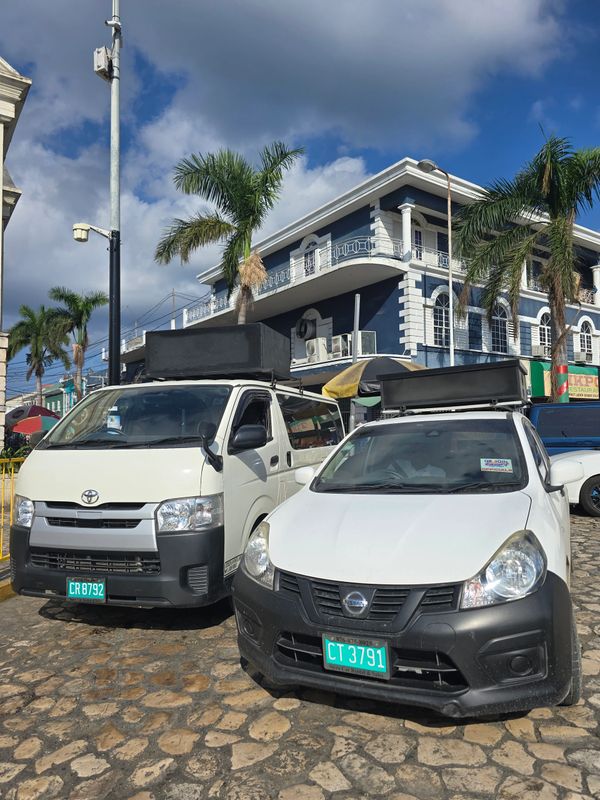 Two white vehicles with rooftop speakers parked on cobblestone street under palm trees.