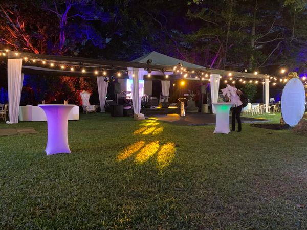 Outdoor event setup with string lights and illuminated tables on grass.