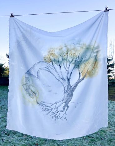 A white cloth with a tree and human  art hanging outdoors.