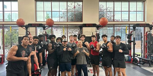 Group of young athletes and coaches posing in a gym with boxing gloves.
