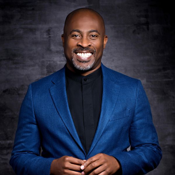 Smiling man in a blue blazer against a dark background.