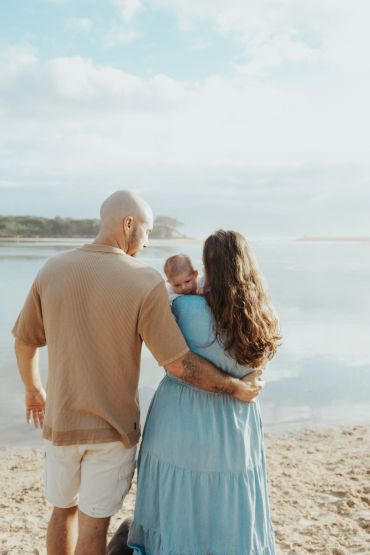 A couple with their baby by a serene lakeside on a sunny day.