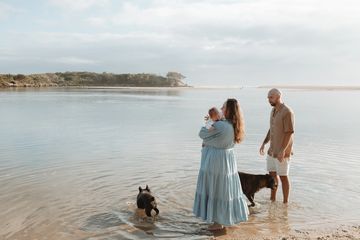 A couple with two dogs standing in shallow water at the beach.