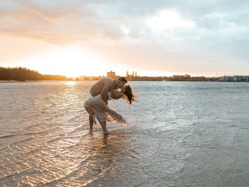 Couple joyfully playing in shallow water at sunset.