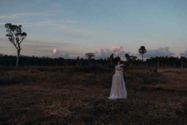 Woman in a white dress stands alone in a vast field at dusk.