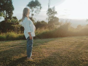 A woman stands barefoot on grass, gazing at the sunrise in a peaceful natural setting.