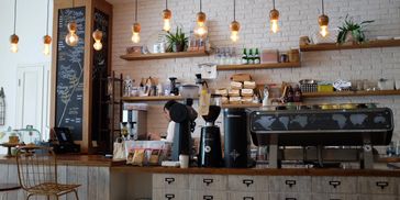 A coffee shop counter with seating. A chalkboard menu titled "Coffee". 