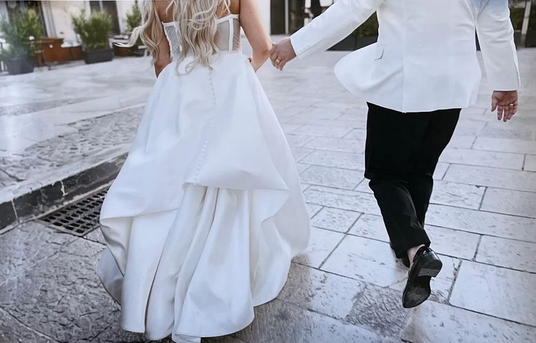 A groom lifts and kisses his bride in a sunlit rustic street.