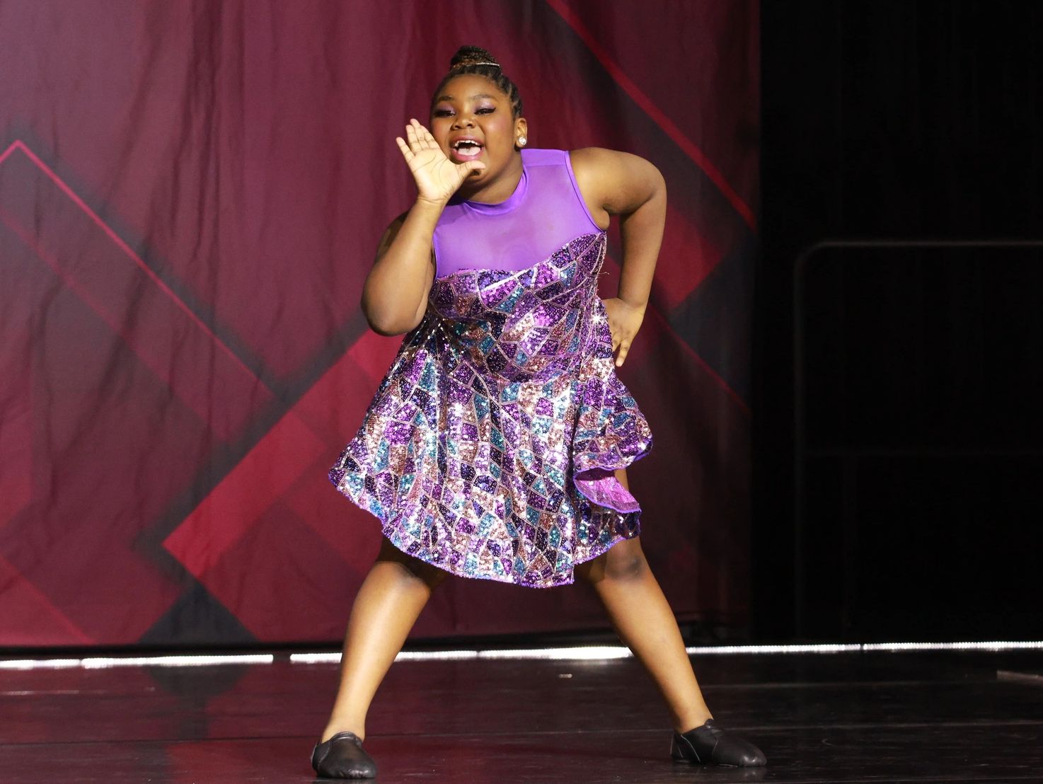 Young girl passionately dancing on stage in a purple dress.