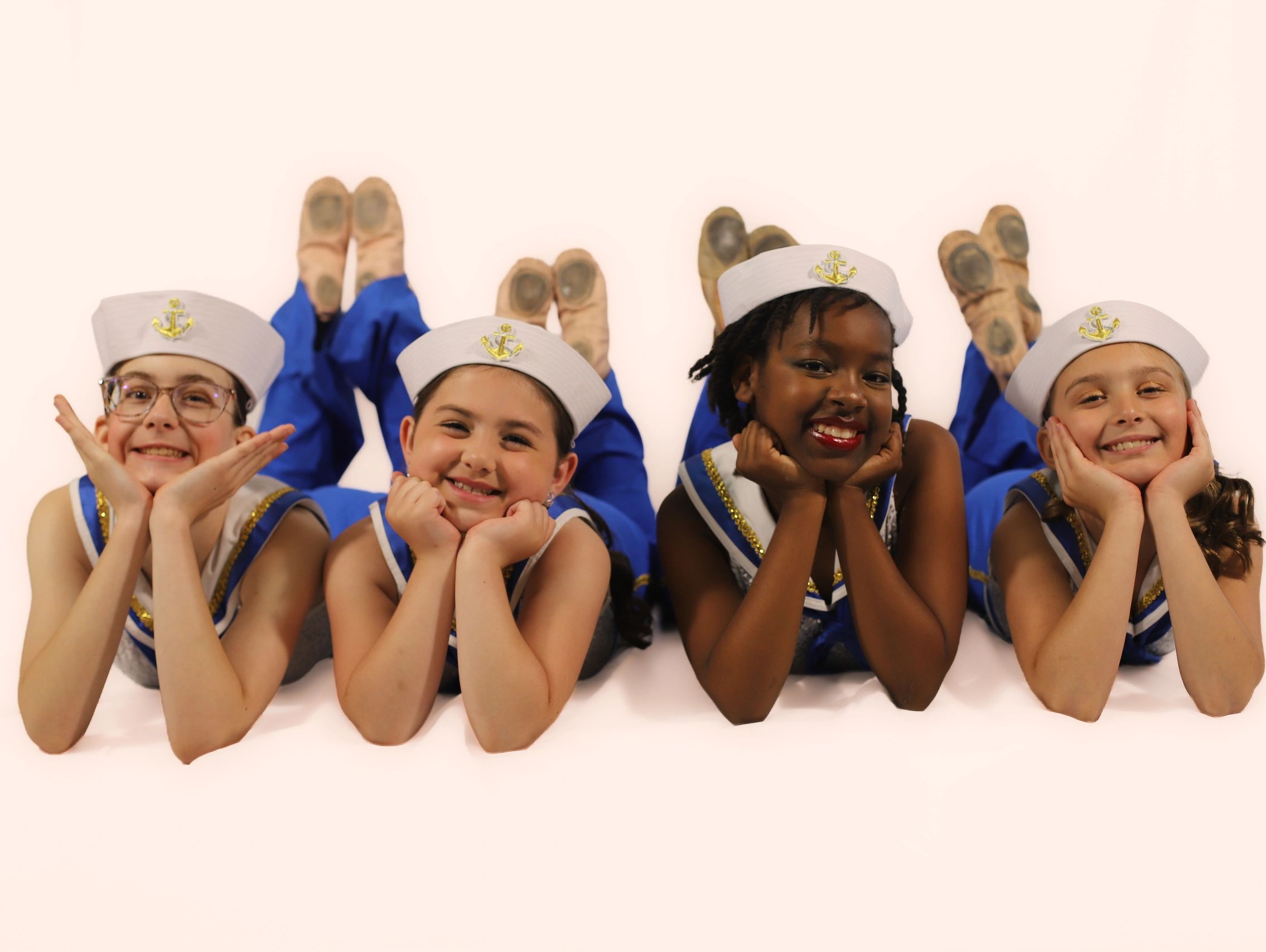 Four kids in sailor outfits smiling with hands on cheeks.
