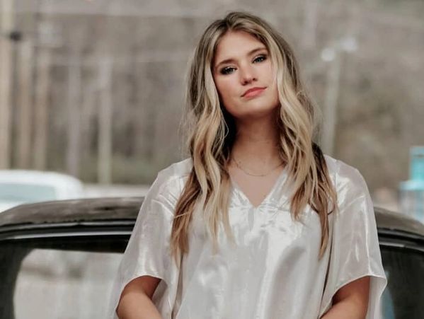 Young woman with long blonde hair wearing a silky white blouse.
