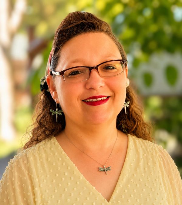 Smiling woman with glasses and dragonfly jewelry.