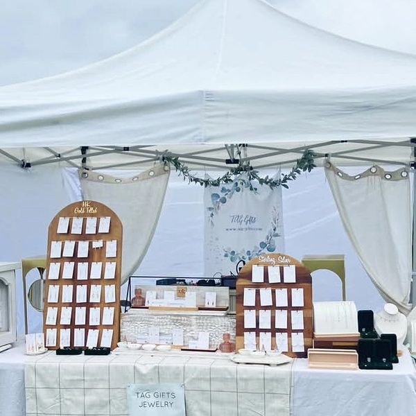 Outdoor jewelry booth under a white canopy with organized displays and greenery.