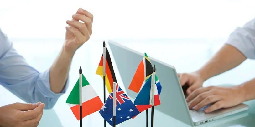 Small international flags on a desk with two people working on a laptop.