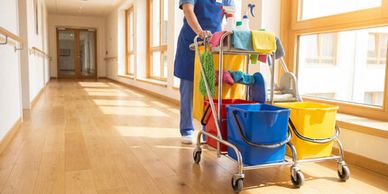 A janitor pushes a cleaning cart in a sunlit hallway.