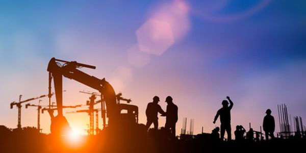 Silhouettes of construction workers and machinery at sunset on a building site.
