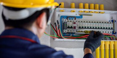 Electrician working on a circuit breaker panel with safety gear.