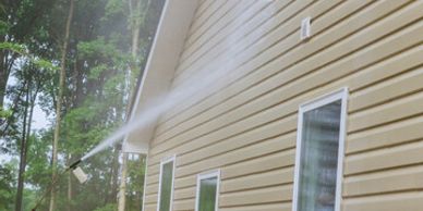 A person pressure washing the siding of a yellow house outdoors.