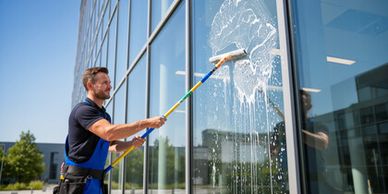 Man cleaning large glass windows with a roller brush.