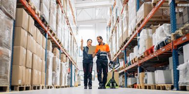 Two workers discussing in a large warehouse aisle surrounded by shelves.