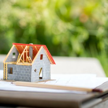 A small model house under construction on architectural plans.