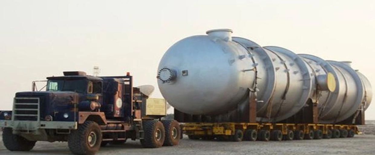 Large truck transporting an enormous cylindrical industrial vessel on a multi-wheeled trailer.