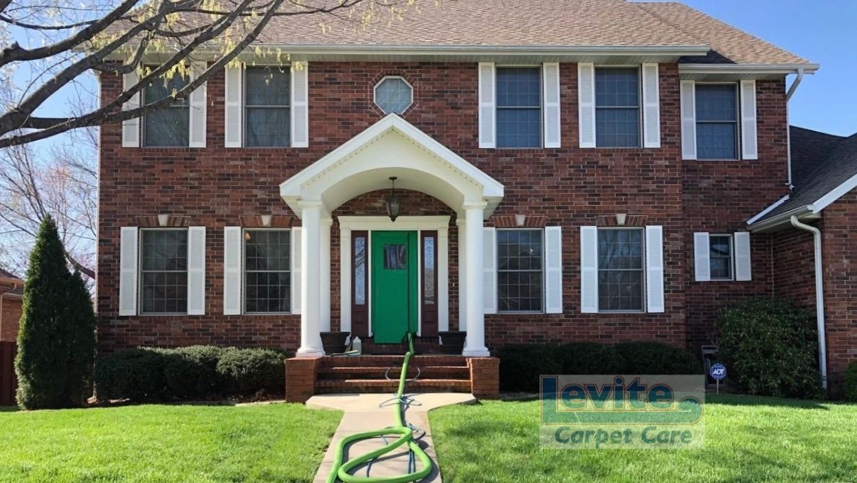 Brick house with a green door and garden hose on the lawn.