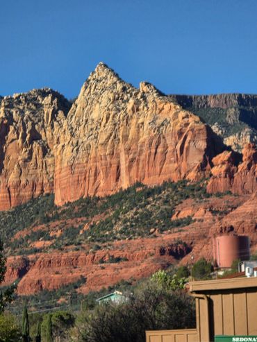 Rocky mountain with red and orange hues under a clear blue sky.