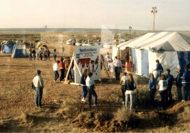 A group of people gathered at a tent in a dry, open area with several smaller tents around.