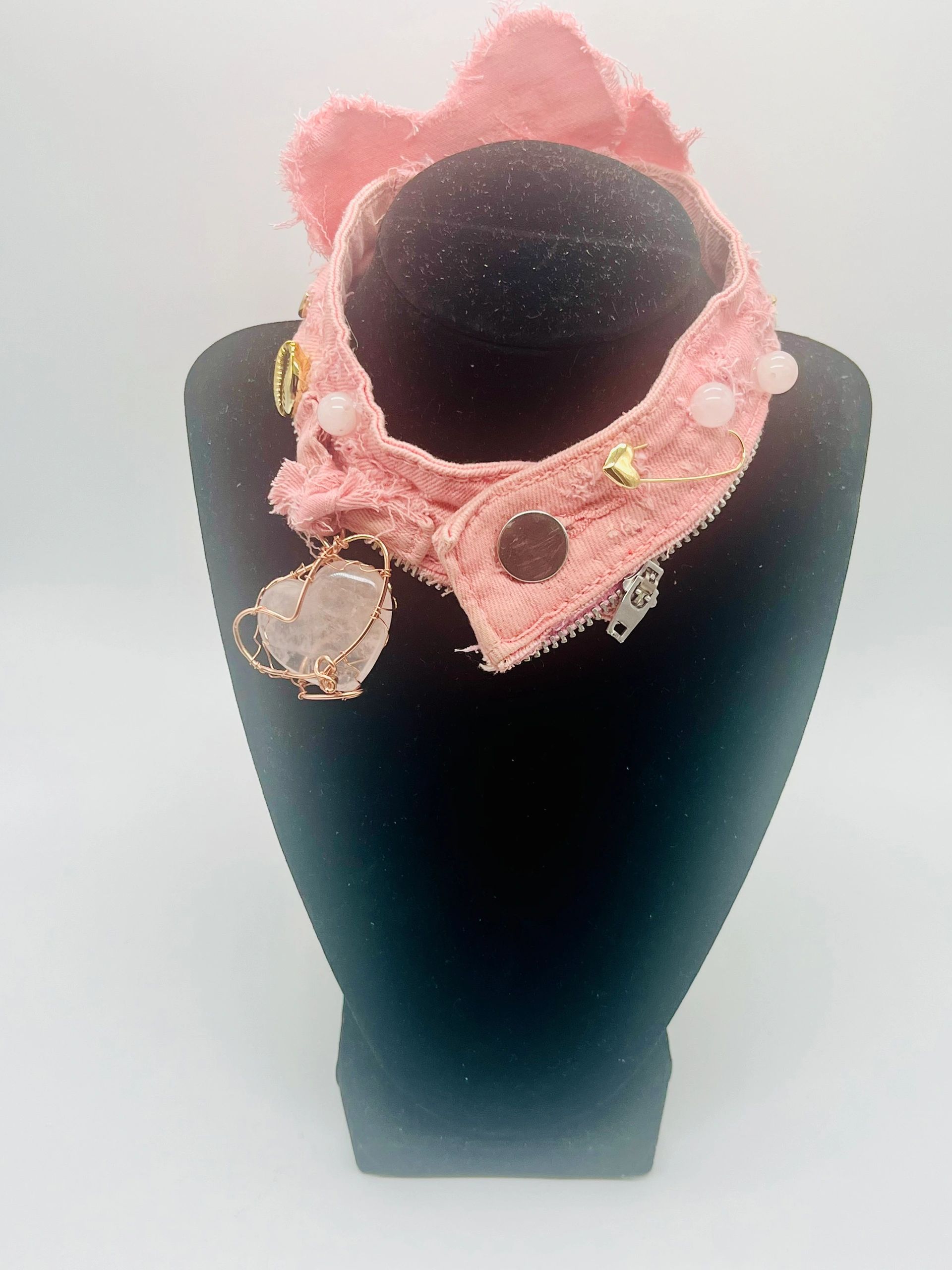Pink fabric necklace with decorative charms on a black mannequin.